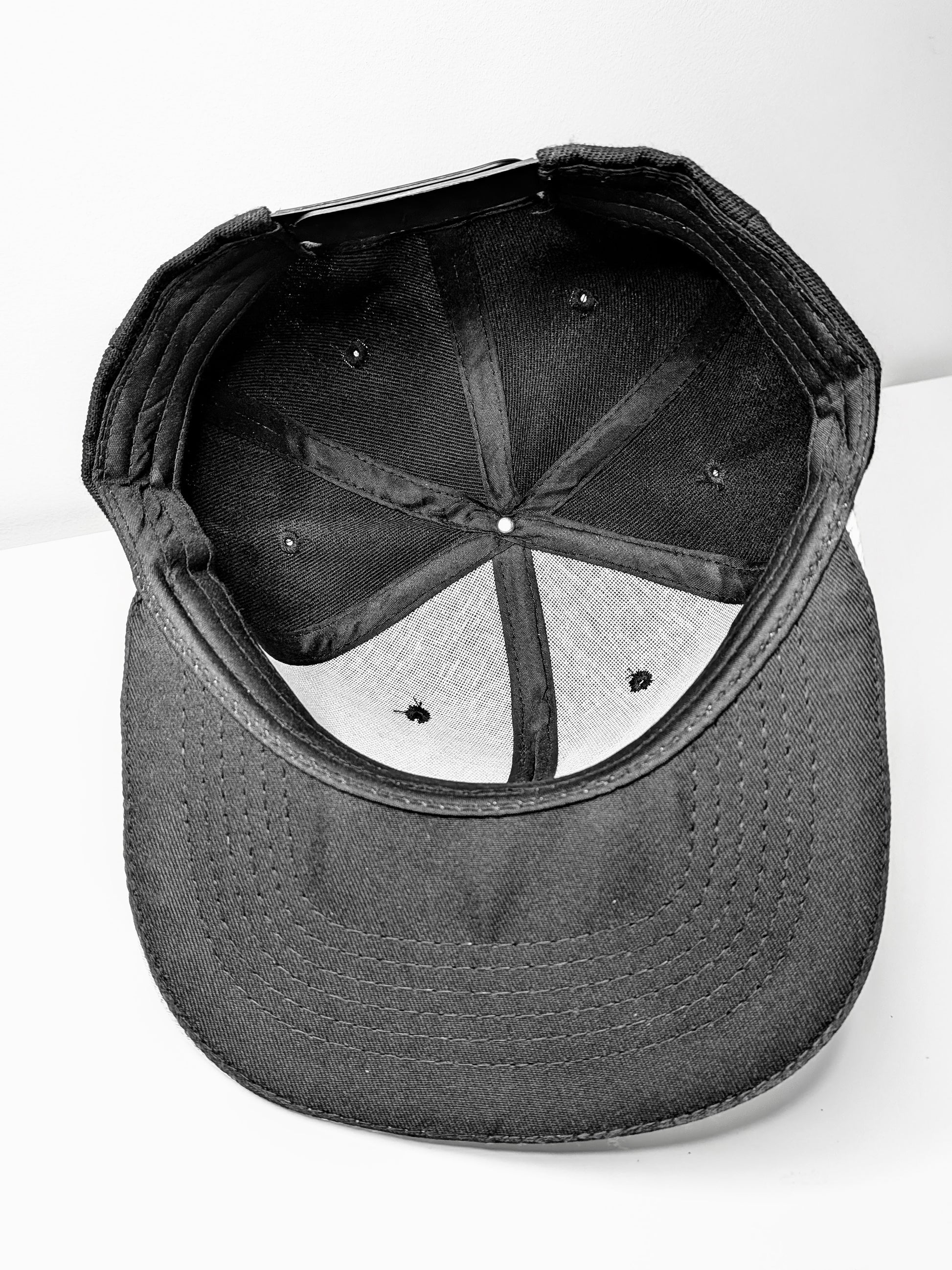 Underside of a black flat brim snap back cap